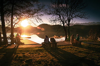 Silhouetted People Relaxing on Benches by Lake at Golden Hour Sunset