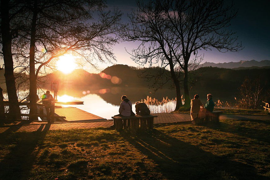 Silhouetted People Relaxing on Benches by Lake at Golden Hour Sunset
