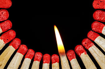 Single lit matchstick surrounded by unlit matches on black background