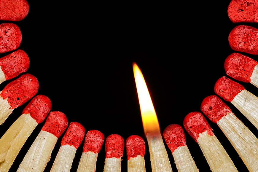 Single lit matchstick surrounded by unlit matches on black background