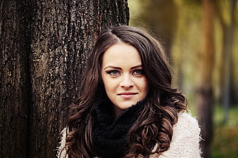 Young woman portrait leaning against tree in autumn park