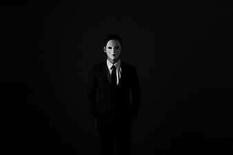 Man in Black Suit Wearing White Guy Fawkes Mask on Black Background