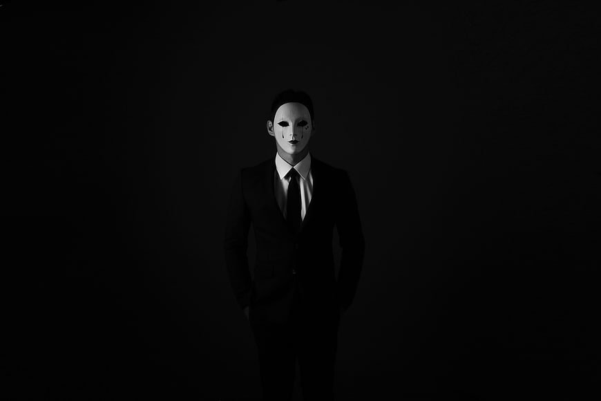 Man in Black Suit Wearing White Guy Fawkes Mask on Black Background