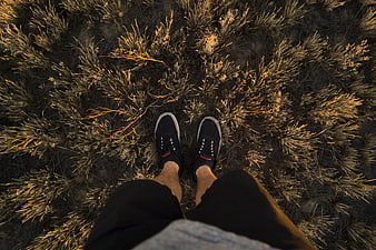 First-person view of black sneakers on dry grass