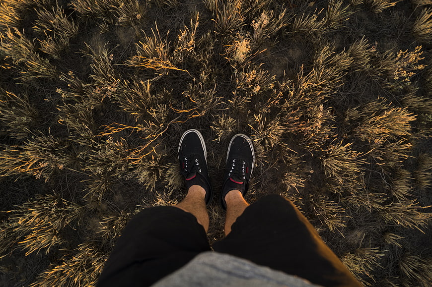 First-person view of black sneakers on dry grass