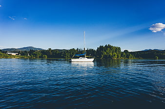 White sailboat on calm blue lake with mountains