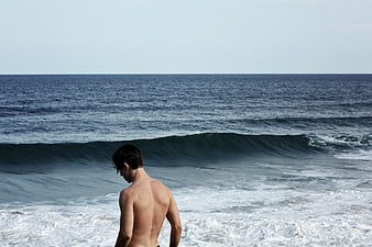 Shirtless Man Looking at Ocean Waves on Beach