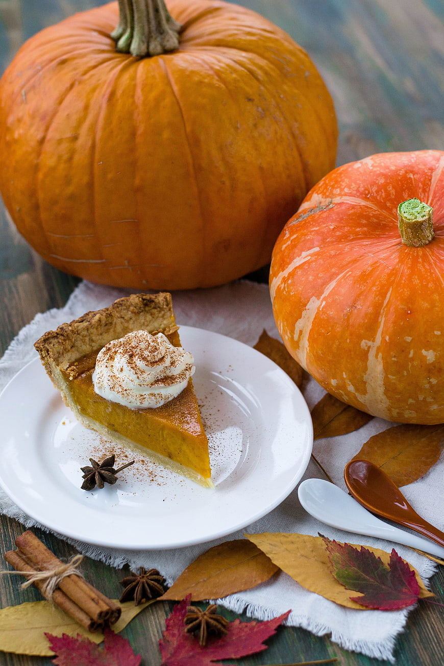 Pumpkin Pie Slice with Whole Pumpkins and Autumn Leaves