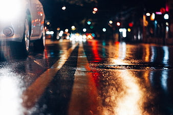 Low angle wet city street at night with car and bokeh lights