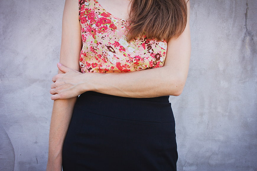 Woman in Floral Top and Black Skirt Against Concrete Wall