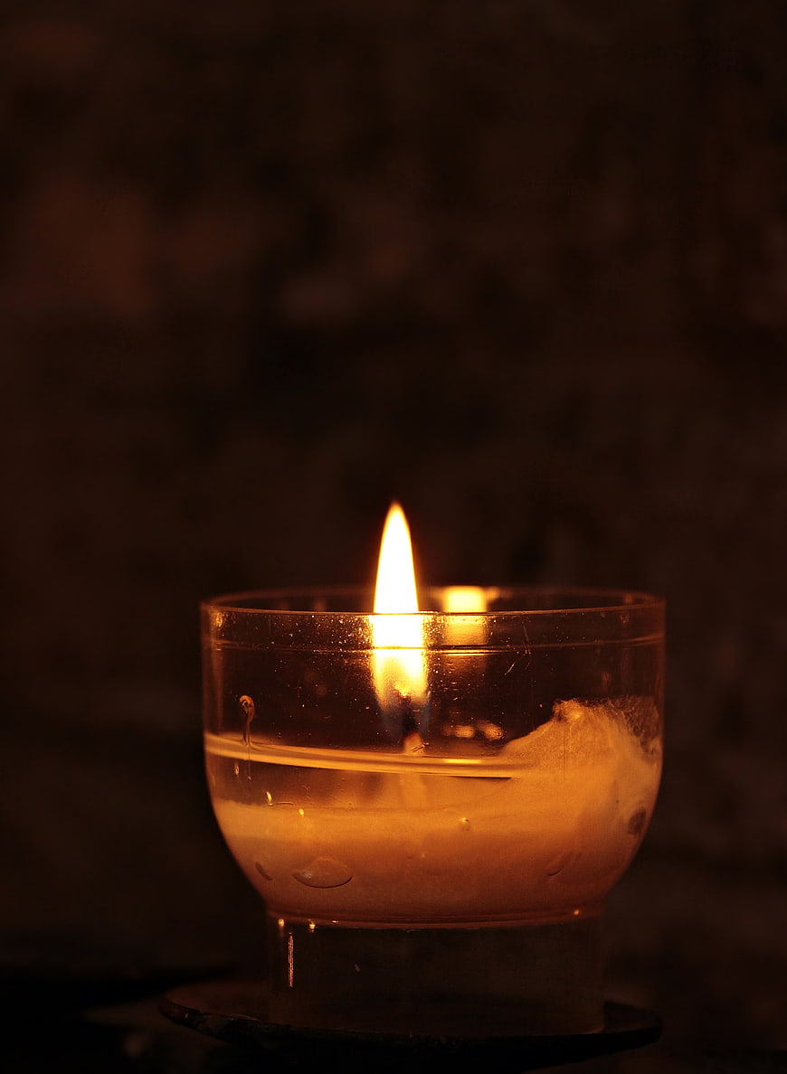 Glowing Tea Light Candle in Glass Holder on Dark Background