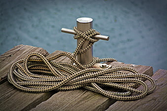 Coiled rope tied to metal bollard on wooden dock