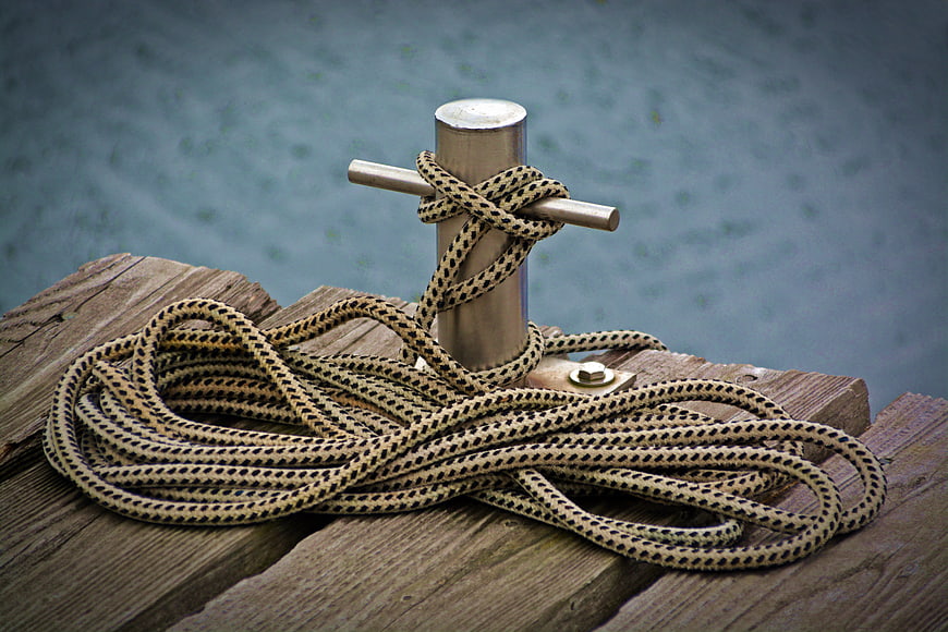 Coiled rope tied to metal bollard on wooden dock