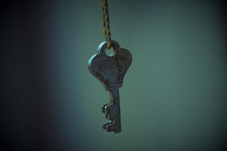 Antique metal key hanging from a rope against a dark background