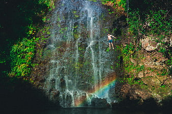 Man rappelling down a lush waterfall with rainbow