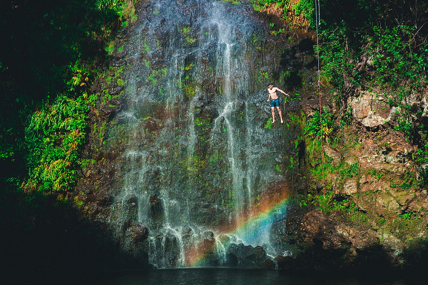 Man rappelling down a lush waterfall with rainbow