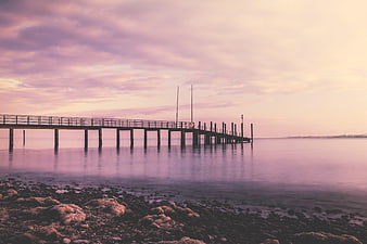 Serene purple sunset over a long pier extending into calm ocean waters