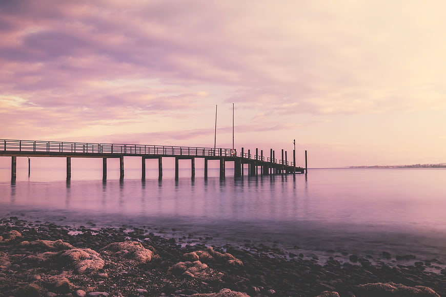 Serene purple sunset over a long pier extending into calm ocean waters