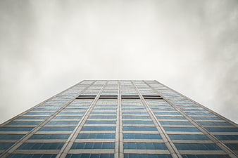 Low angle view of modern glass skyscraper against cloudy sky