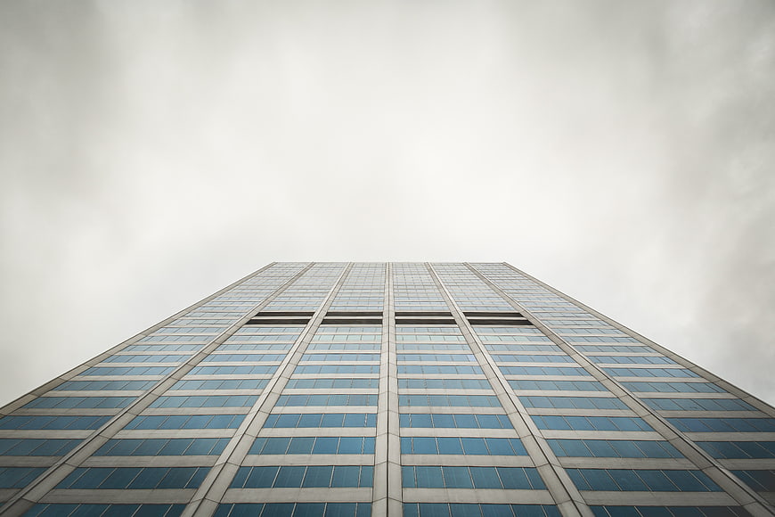 Low angle view of modern glass skyscraper against cloudy sky
