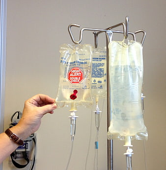 Hand adjusting IV drip bag with high alert label on hospital stand