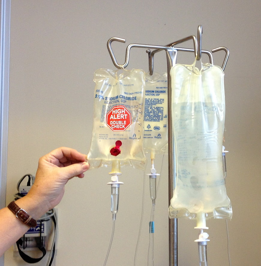 Hand adjusting IV drip bag with high alert label on hospital stand