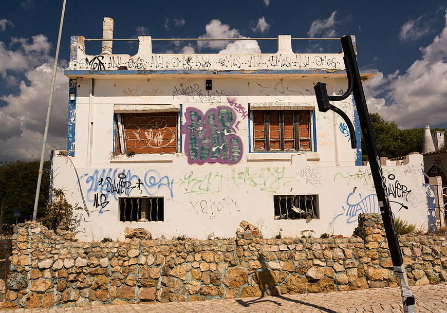 Abandoned white building with colorful graffiti and stone wall