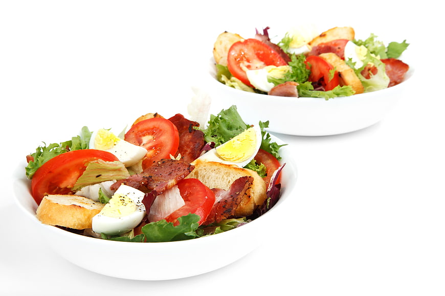 Two bowls of fresh salad with bacon, egg, and tomato on white background