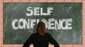 Woman standing before chalkboard with self confidence written