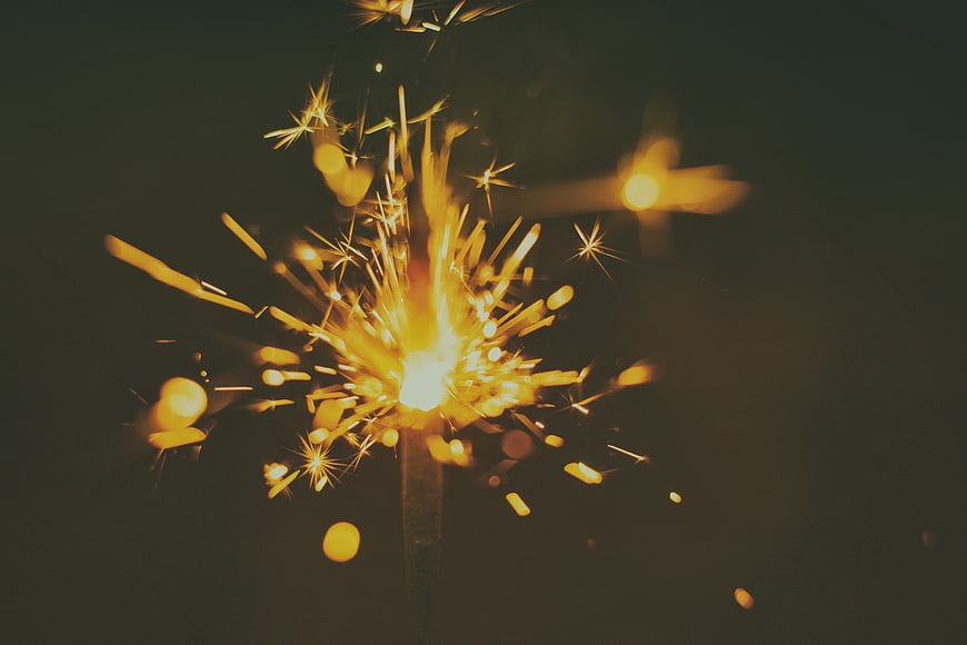 Burning Sparkler with Golden Sparks Against Dark Night Background