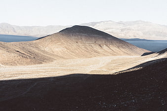 Arid desert landscape with central hill and distant blue lake
