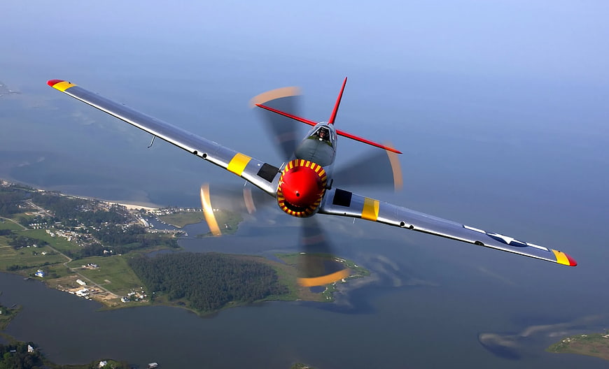 Vintage Silver Propeller Plane Flying Over Coastal Landscape