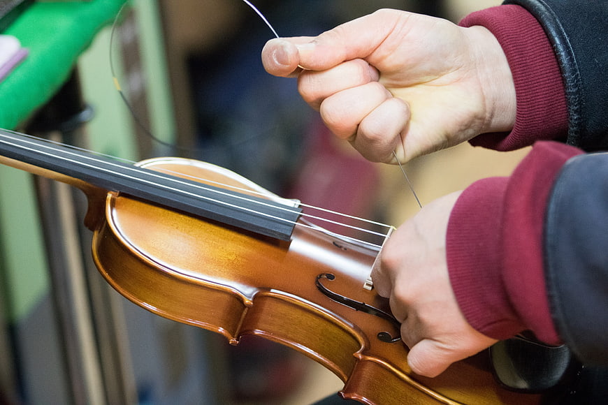 Close-up of hands repairing a violin string in a workshop