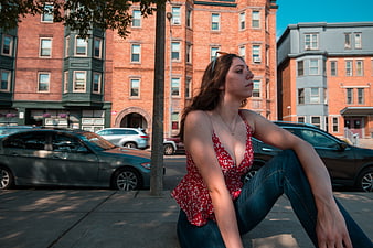 Young woman sitting on city sidewalk in red floral top