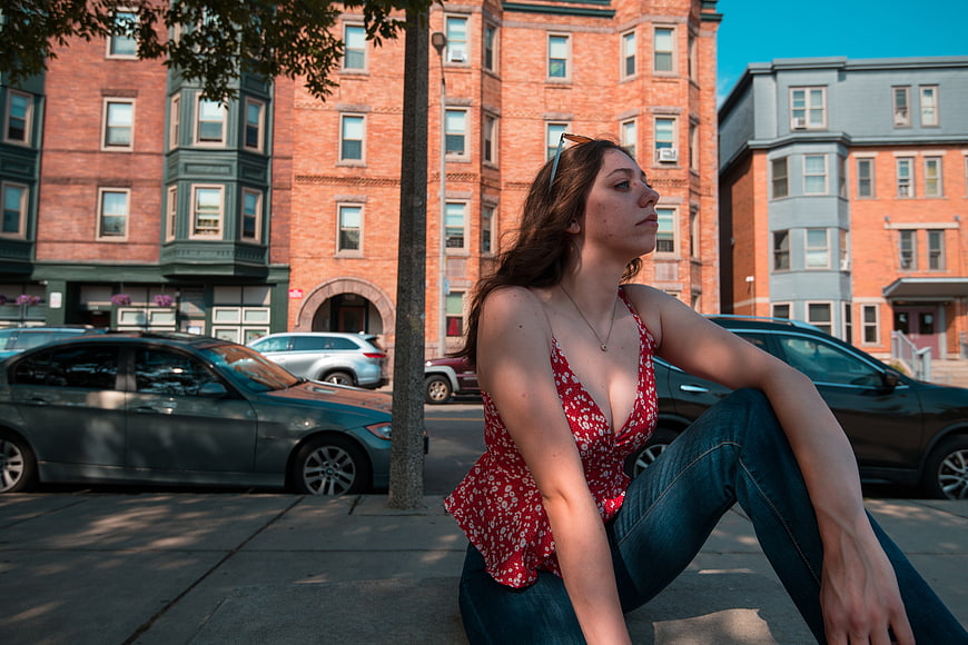 Young woman sitting on city sidewalk in red floral top