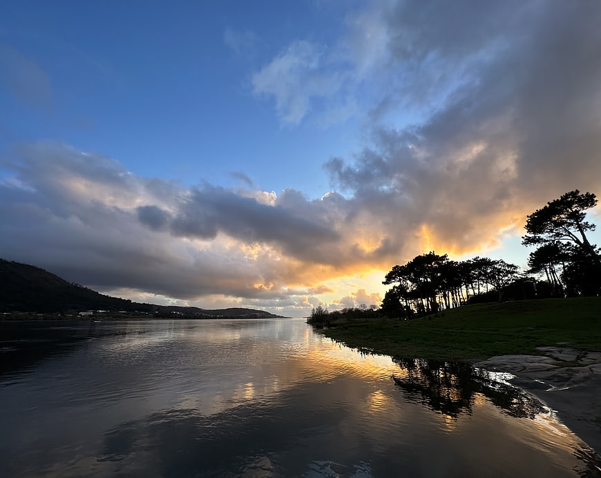 Dramatic sunset over calm river with tree silhouettes