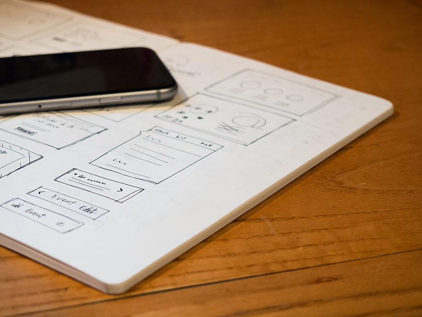 Hand-drawn mobile app wireframes on notebook with smartphone