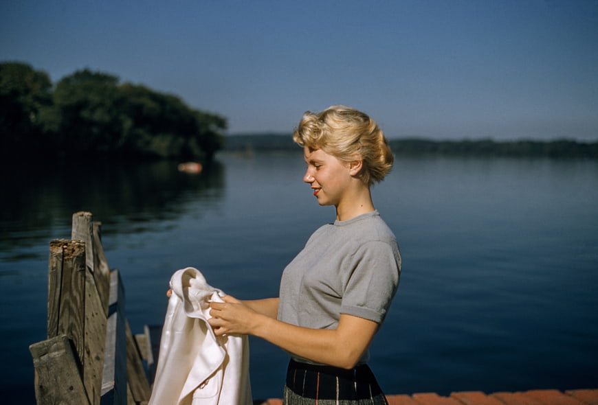 Vintage blonde woman holding white jacket by lake