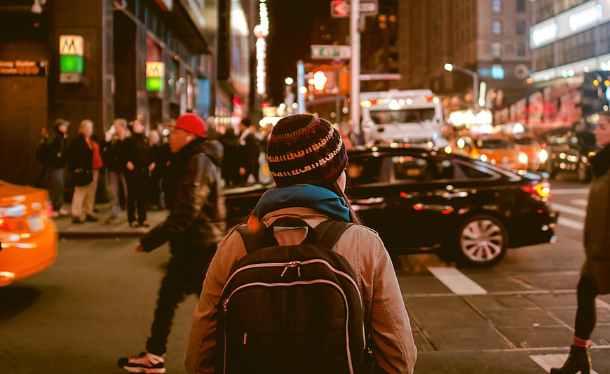 Back view of person with backpack in busy city street at night