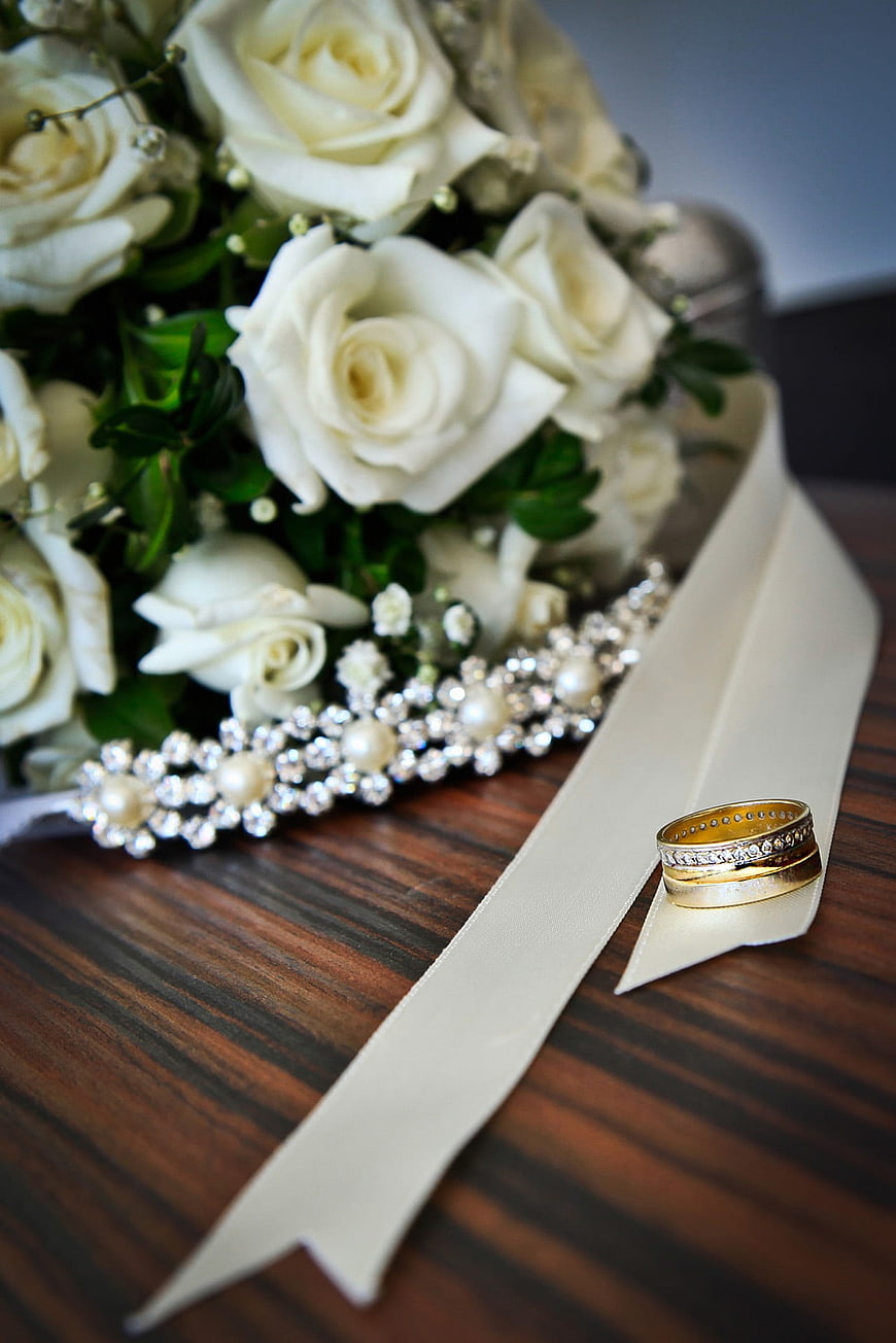 Wedding Rings and White Rose Bouquet on Wooden Table