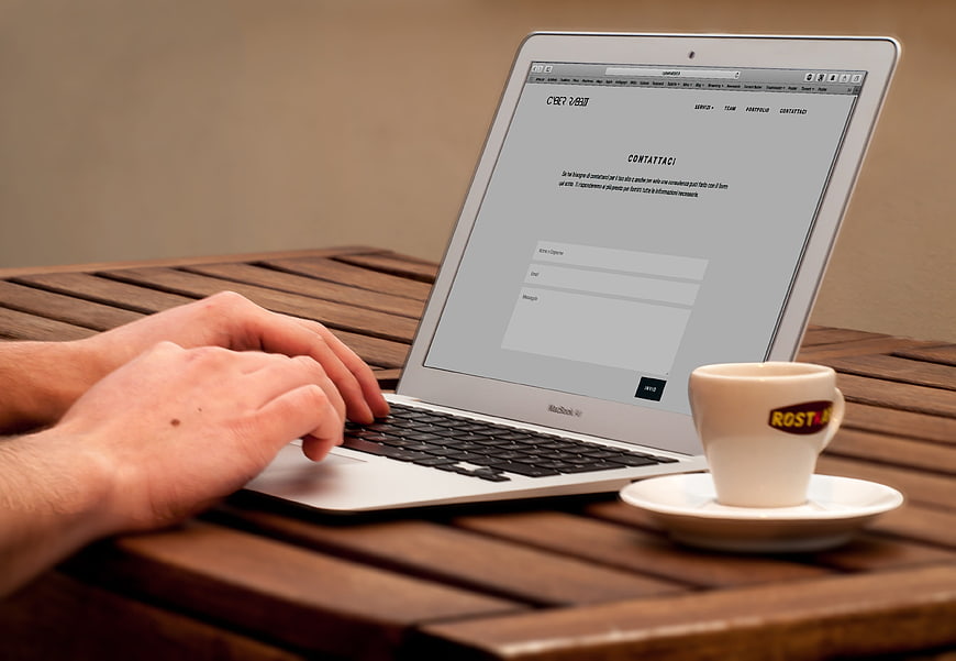 Hands typing on laptop with espresso cup on wooden table