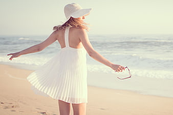 Woman in White Dress and Hat Walking on Beach