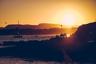 Silhouetted Group Watching Golden Sunset Over Ocean with Sailboat