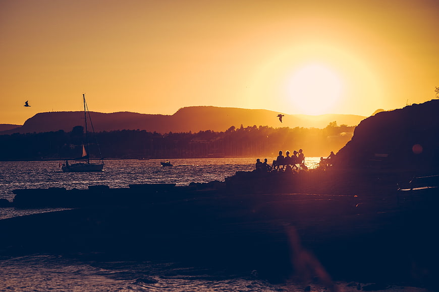 Silhouetted Group Watching Golden Sunset Over Ocean with Sailboat
