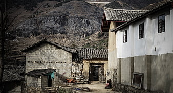 Rural village houses near mountain cliff with woman sitting