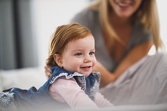 Smiling toddler girl lying on bed with mother in background