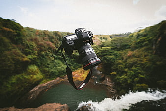 Black DSLR Camera Hanging Over Lush Waterfall Canyon