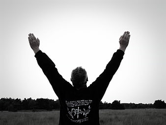 Man with raised arms in field, black and white religious worship