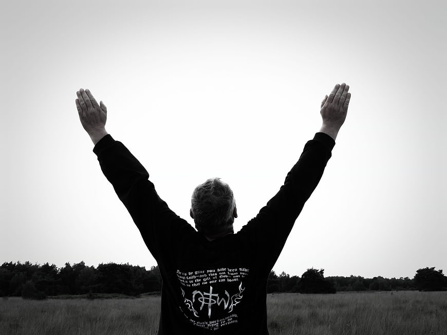 Man with raised arms in field, black and white religious worship