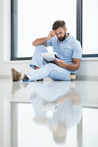 Stressed male nurse sitting on hospital floor reading documents